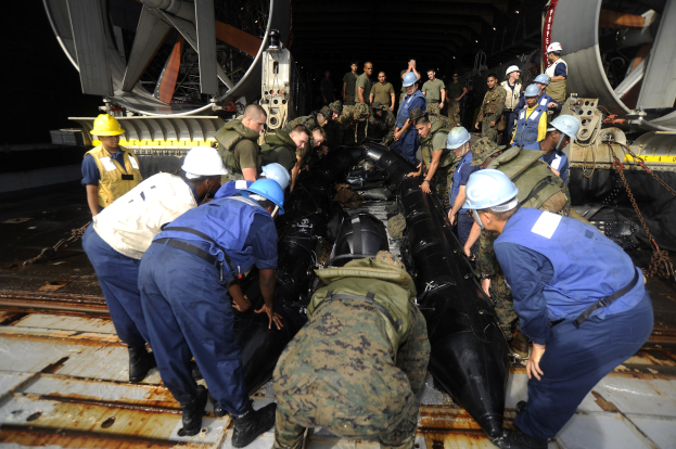 Eine Gruppe von Männern in Helmen und Uniformen, die an einem U-Boot in einem Schiffbauwerk arbeiten.