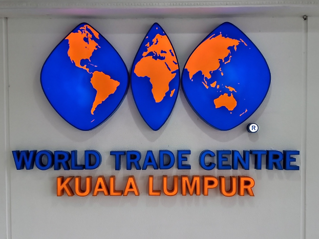 Das Logo des World Trade Centre in Kuala Lumpur, Malaysia, auf einer Wand mit fetter schwarzer Schrift und einem weißen Rand vor einem hellblauen Himmel mit weißen Wolken.
