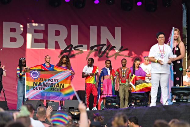 Gruppe von Menschen auf einer Bühne mit einem Banner, auf dem 'Berlin as Fuck' steht, mit Lautsprechern, Mikrofonen und einer Menge darunter, die ihre Hände hebt.