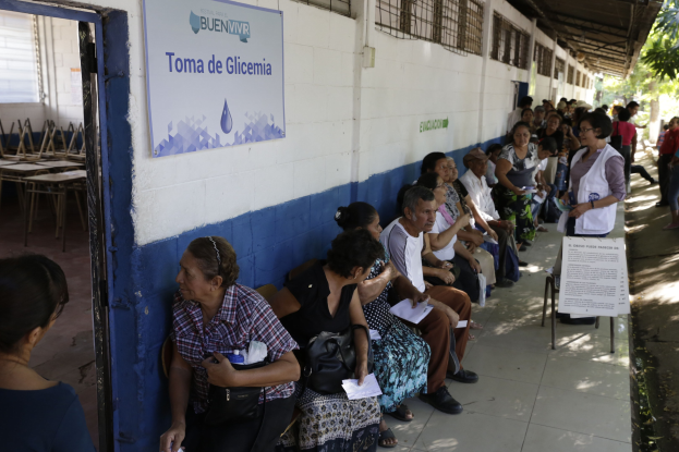 Menschen sitzen auf Bänken vor einem Gebäude, warten in der Schlange, um bei einer Wahlurne in Guadalajara, Mexiko, zu wählen, mit einem Schild an der Wand und Bäumen im Hintergrund.