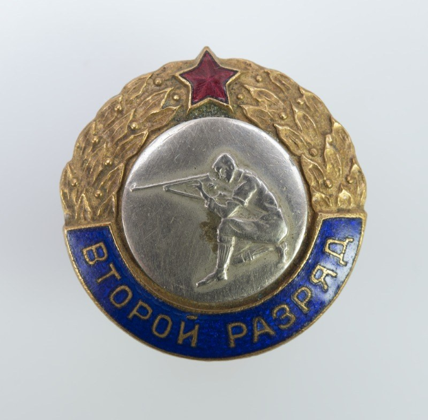 Ein russisches Militärabzeichen mit einem zentralen roten Stern und umgebendem Text.