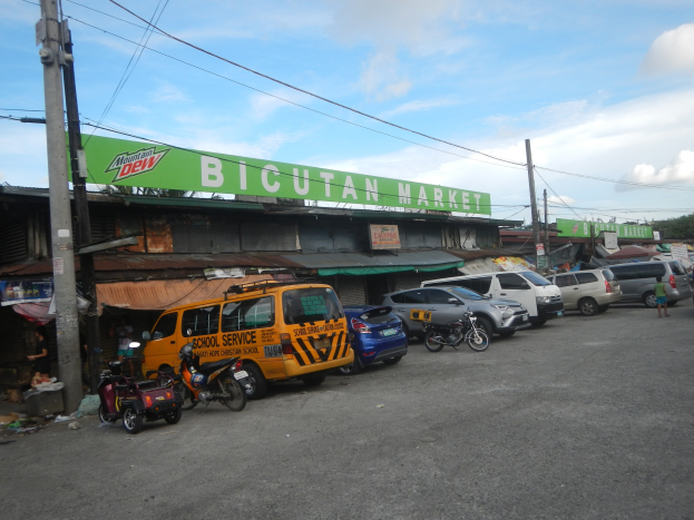 Ein belebter Straßenmarkt in Cebu City, Philippinen, mit Fahrzeugen, Fußgängern, Strommasten, Gebäuden, Bäumen und einem bewölkten Himmel.