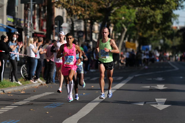 Gruppe von Menschen, die bei einem Marathon auf einer Stadtstraße laufen, mit Zuschauern im Hintergrund.
