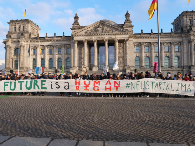 Eine Gruppe von Menschen steht vor dem Reichstagsgebäude in Berlin und hält eine Fahne mit der Aufschrift "Zukunft ist menschlich" in der Hand.