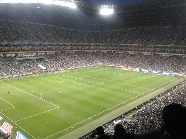 Ein hell erleuchtetes Fußballstadion voller jubelnder Zuschauer, umgeben von Werbetafeln.