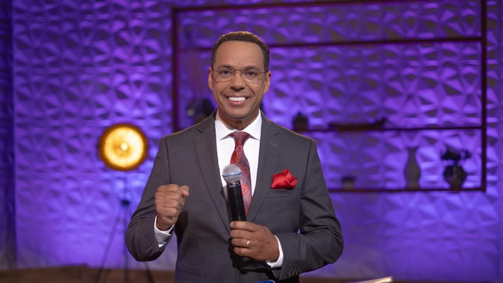 Stephen Colbert, Moderator von 'The Daily Show with Trevor Noah', steht auf einer Bühne und hält ein Mikrofon in der Hand, trägt einen Anzug, Krawatte und Brille, mit einem Scheinwerfer und Ständer hinter ihm.