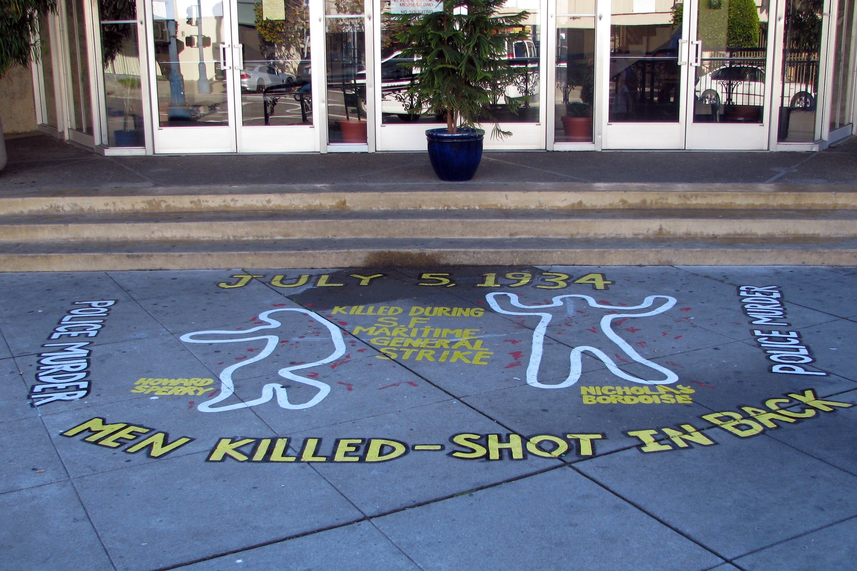 Ein Gebäude mit Glastüren und Fenstern, einem Topf mit einer Pflanze und einem Bürgersteigschild, auf dem 'Männer erschossen' steht.