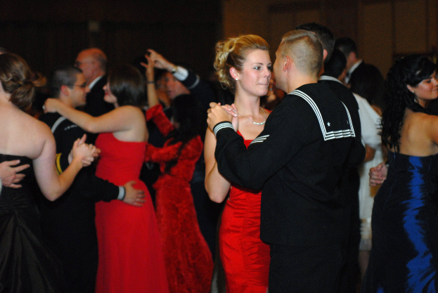 Gruppe von formell gekleideten Menschen, die energisch auf einer Tanzfläche tanzen, mit einer Wand im Hintergrund.