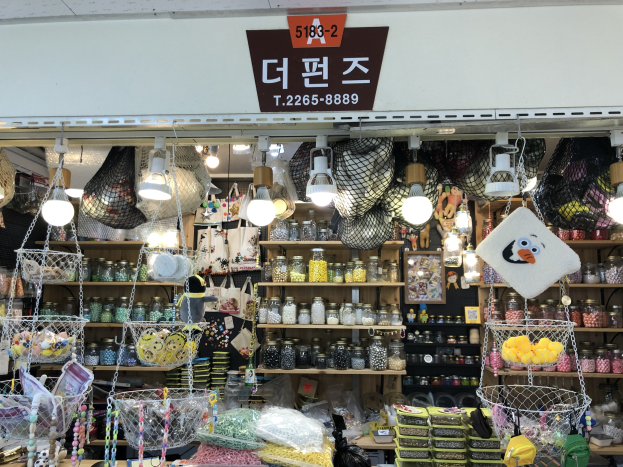 Ein unordentlicher Laden in Seoul zeigt verschiedene Gegenstände wie Körbe, Lichter, Flaschen und Spielzeuge auf Regalen, mit einer Tafel oben, die ihn als einen der besten koreanischen Läden kennzeichnet.