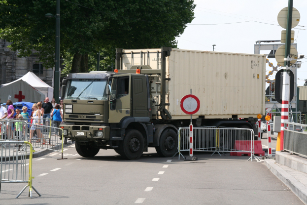 Ein Lkw parkt am Straßenrand, umgeben von einer Gruppe von Menschen auf dem Bürgersteig, umgeben von verschiedenen städtischen Elementen unter einem klaren blauen Himmel.