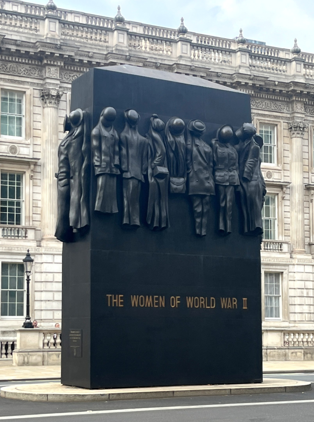 Schwarzer Granitdenkmal mit eingravierter Inschrift, umgeben von einer Straße, Laternen, Geländern und einem Gebäude im Hintergrund unter einem bewölkten Himmel.