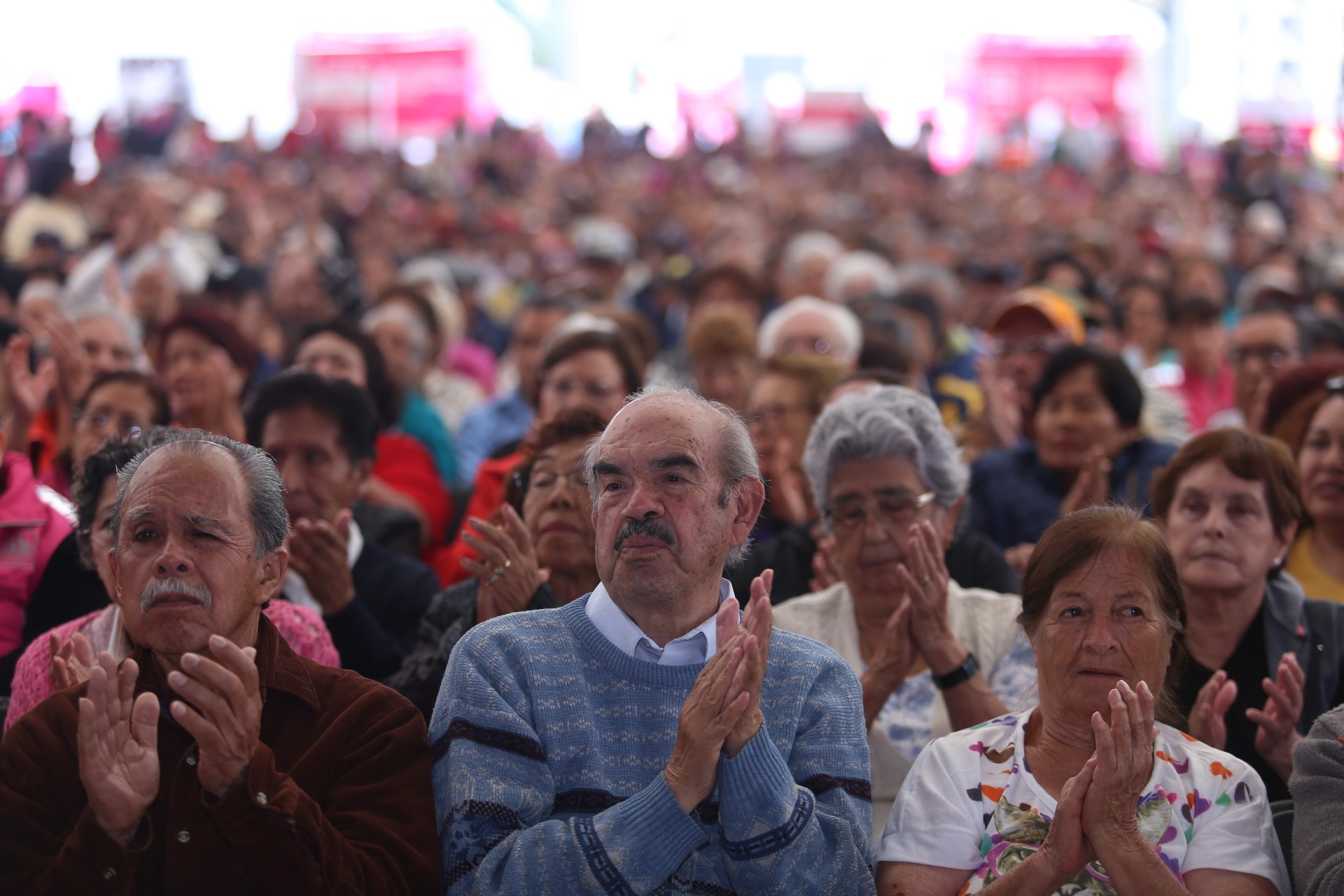 Eine große Gruppe von Menschen, die mit gefalteten Händen beten, vor einer Menge sitzend, mit einem unscharfen Hintergrund.
