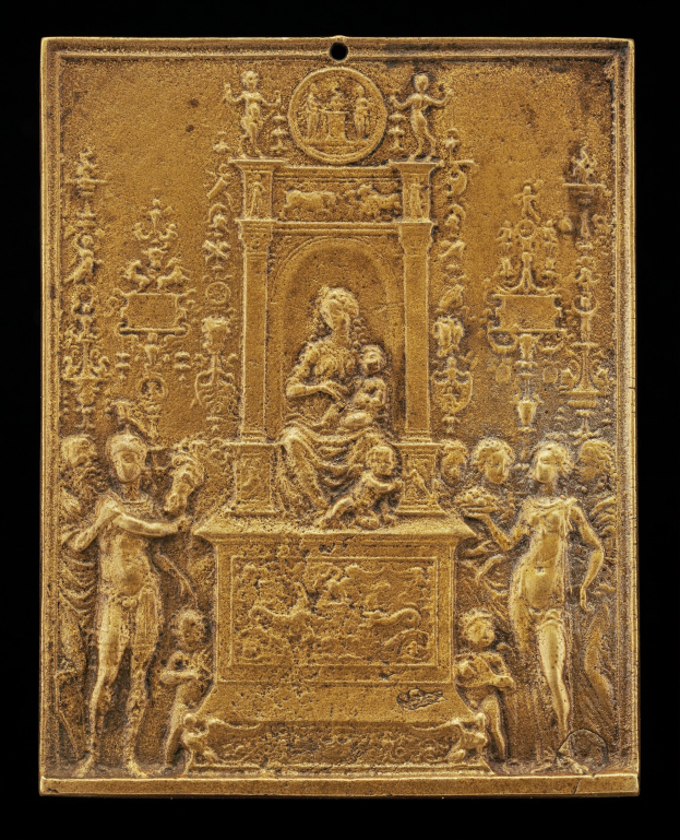 Eine goldene Plakette mit einer detaillierten Skulptur einer Frau in einem langen Kleid und eines Mannes in Anzug und Krawatte, eingerahmt von einem prunkvollen goldenen Rand vor einem schwarzen Hintergrund.