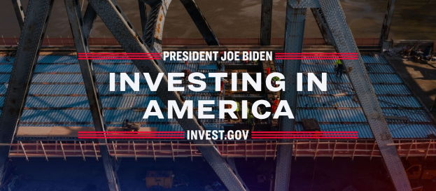 Präsident Joe Biden steht neben einer Brücke mit dem Text "In America investieren" und verstreuten Gegenständen im Vordergrund.