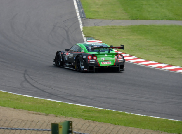 Nissan GT-R Nismo GT3 Rennauto auf der Nürburgring 24 Stunden Strecke, umgeben von grünem Gras und einem Zaun unten.