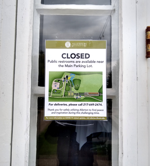 Glasstür mit einem Schild, auf dem "Geschlossene öffentliche Toiletten in der Nähe des Hauptparkplatzes" steht, und einem undeutlichen Objekt auf der rechten Seite.