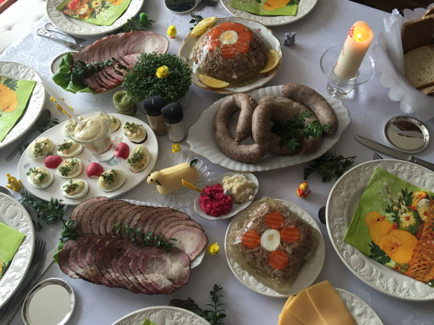 Ein langer Tisch mit verschiedenen Gerichten, Besteck und Kerzen, umgeben von Stühlen, die ein traditionelles deutsches Osteressen darstellen.