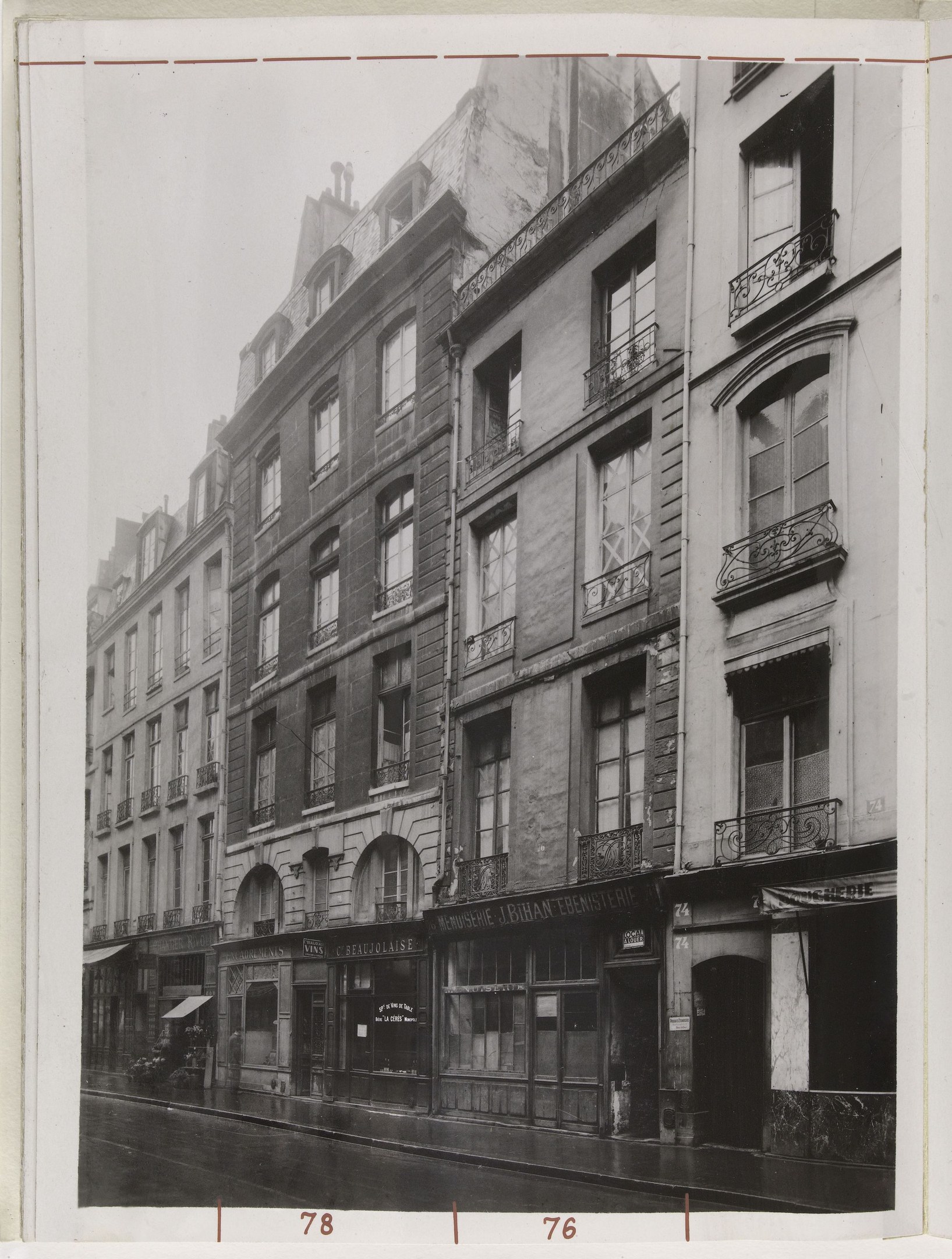 Schwarzes und wei├čes Foto einer Stra├če mit Geb├Ąuden, Fenstern, Gel├Ąndern, Namensschildern und einer Stra├če unten.