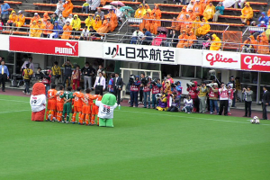 Ein Fußballspiel in einem Stadion mit sechs Spielern, drei Fußballen, vielen Zuschauern in Regenschirmen haltend und mehreren Kameraleuten.