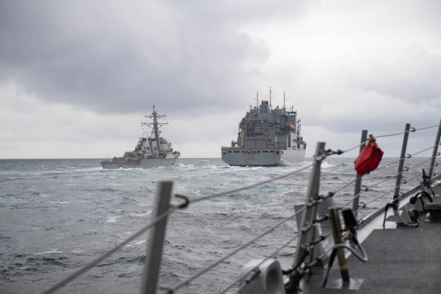 Zwei Schiffe sind im Ozean mit einem bewölkten Himmel im Hintergrund; ein Schiff auf der rechten Seite hat sichtbare Relings und Seile, während sich ein anderes Schiff auf der linken Seite befindet.