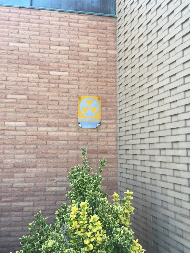 Ein Ziegelbau mit einem Strahlungssymbol-Schild, einer Pflanze am Boden und einer Tafel an der Wand, die anzeigt, dass es ein Kernkraftwerk ist.