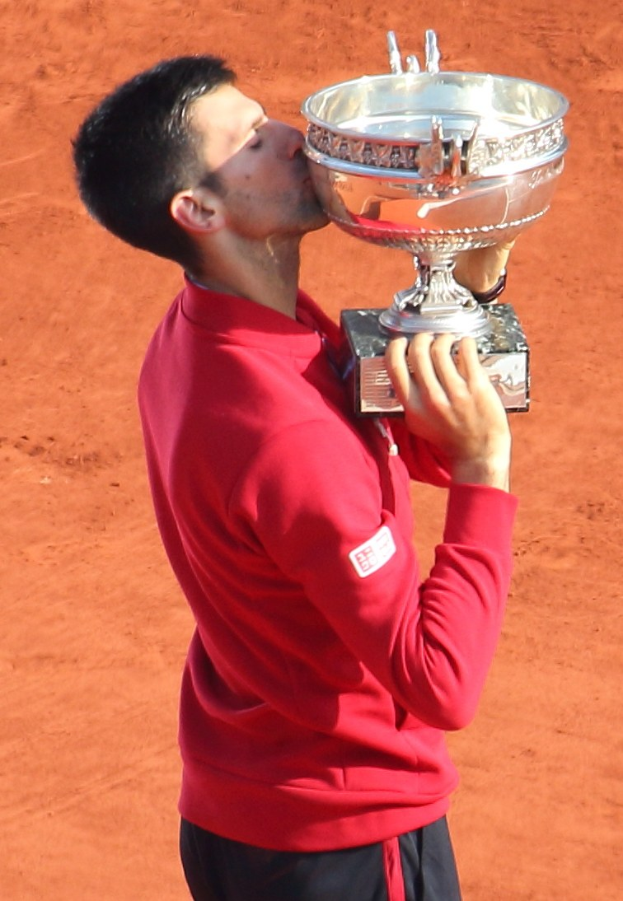 Novak Djokovic hält den French-Open-Pokal nach dem Sieg gegen Rafael Nadal im Finale der Herren-Einzel, feiert mit einem triumphierenden Gesichtsausdruck.