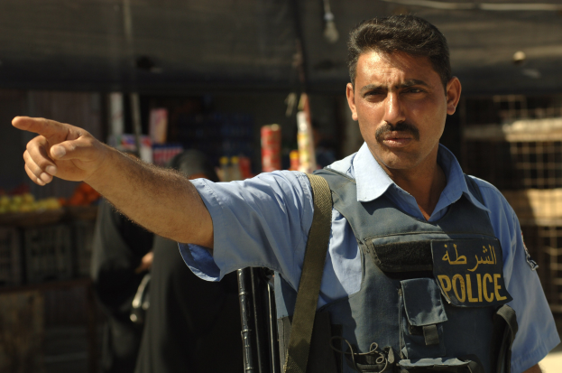 Polizeibeamter in Uniform mit Pistole vor einem Geschäft stehend, mit unscharfen Menschen und Objekten im Hintergrund.