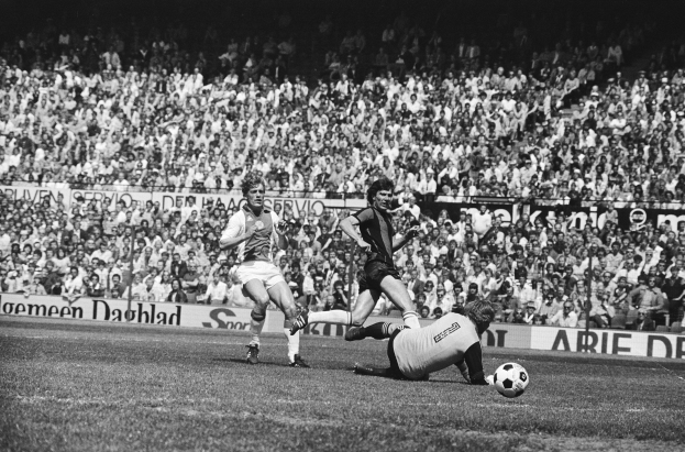 Schwarzes und weißes Foto von Männern, die auf einem Feld Füßball spielen, mit Zuschauern im Hintergrund und einem Banner "Bundesliga 1978-79 Ajax 1-1 Hannover 96"