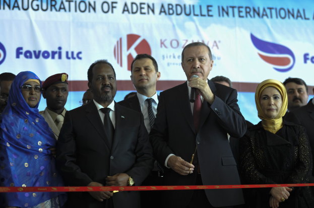 Gruppe von Menschen vor einer roten Schleife mit einem Mann mit Mikrofon, dahinter eine Tafel mit der Aufschrift 'Eröffnung des Aden Abdulle International Airport'.