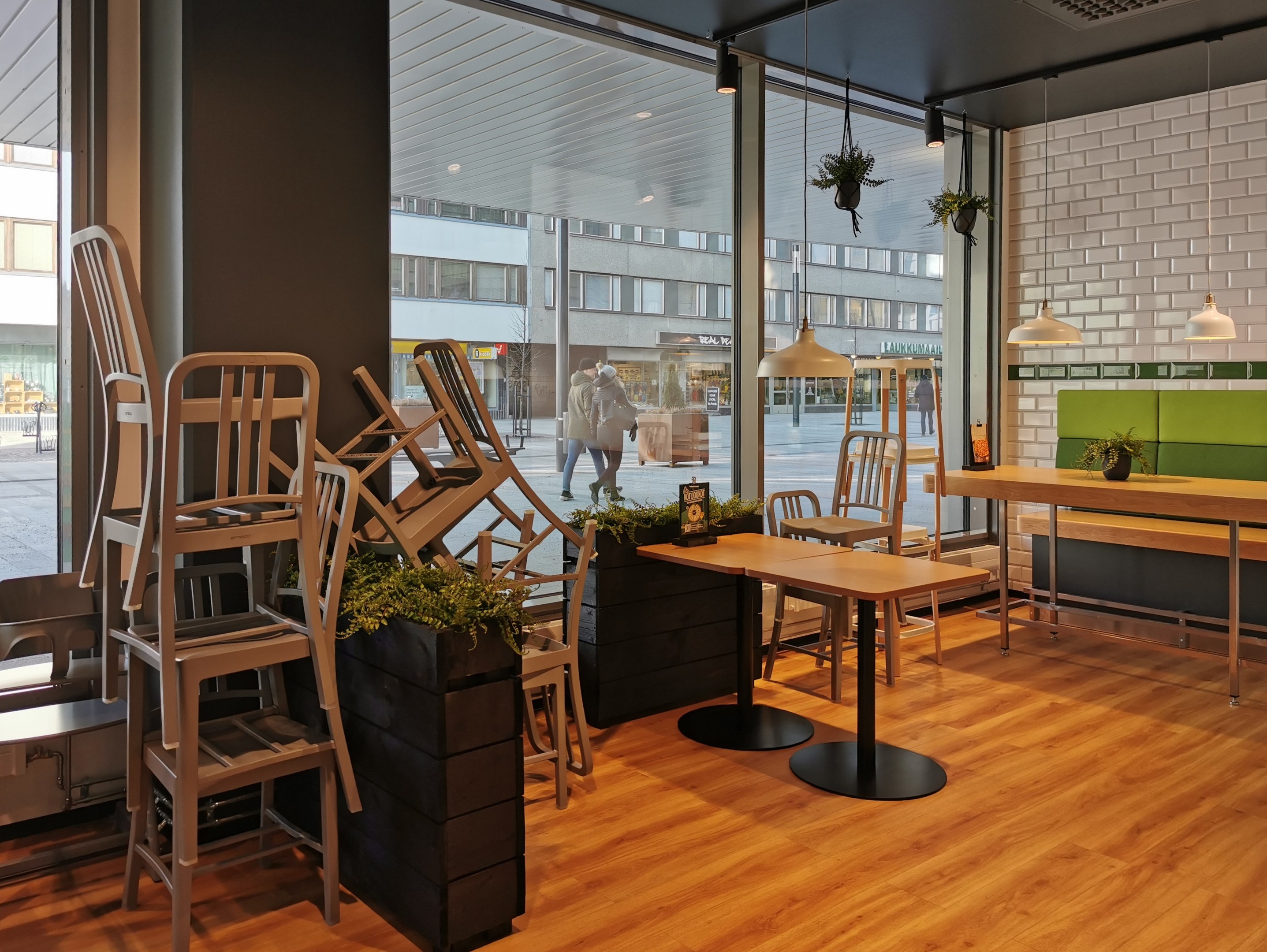 Ein Restaurant in Berlin mit Holztischen und -stühlen in der Nähe eines großen Fensters, das eine Außenansicht von Fußgängern, Gebäuden und städtischen Elementen zeigt.