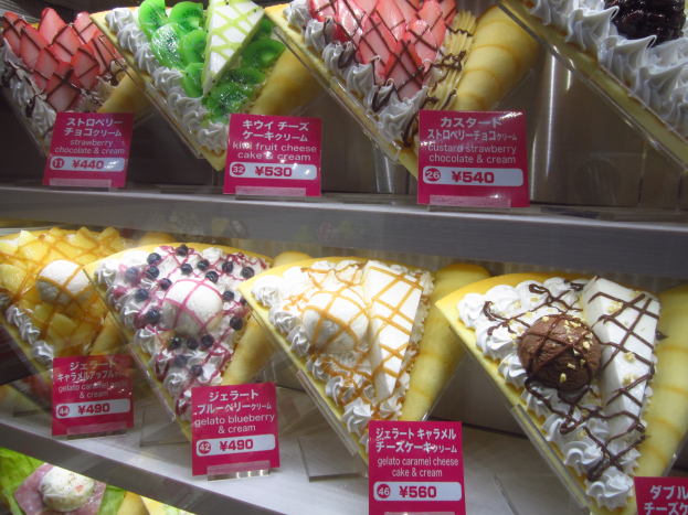 Vitrine voller verschiedener Eissorten, jeweils mit Preisschild, in unterschiedlichen Farben, Formen und Geschmacksrichtungen angeordnet.