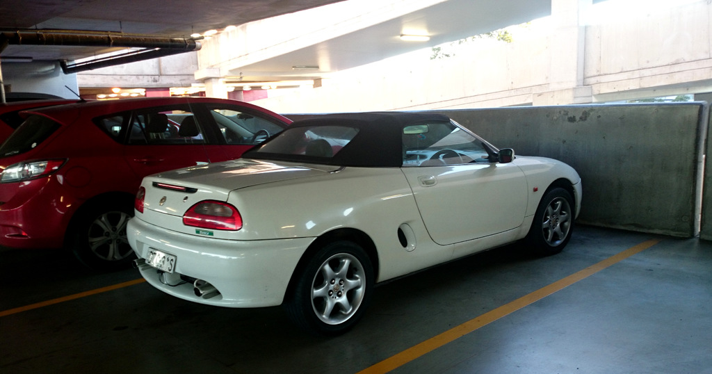 Autos sind in einem Keller mit einem Rohr am Dach und einem weiteren Gebäude oben rechts geparkt.