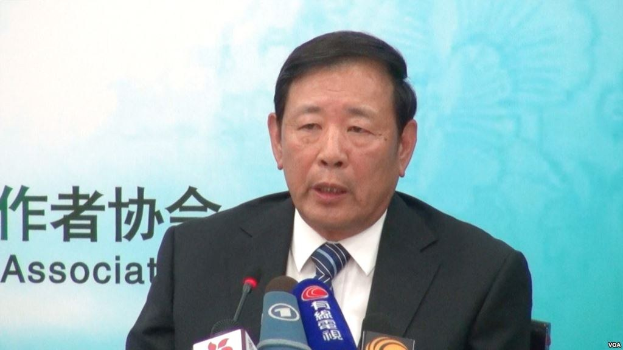 Ein Mann in Anzug und Krawatte sitzt an einem Tisch mit Mikrofonen und spricht hinter einem Banner, wahrscheinlich zu der Nachricht über Chinas Präsidenten Hu Jintao.