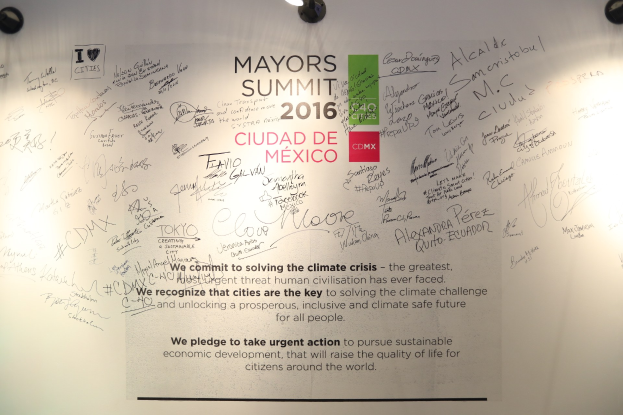 Weiße Wand mit einem Schild, auf dem "MAYORS SUMMIT 2016" steht, beleuchtet von Deckenleuchten.