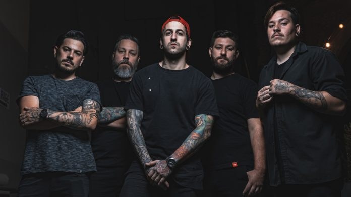 Gruppe von Männern, die in einem schwach beleuchteten Raum während eines Interviews stehen, wahrscheinlich für Avenged Sevenfold.