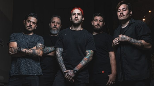 Gruppe von Männern, die in einem schwach beleuchteten Raum während eines Interviews stehen, wahrscheinlich für Avenged Sevenfold.