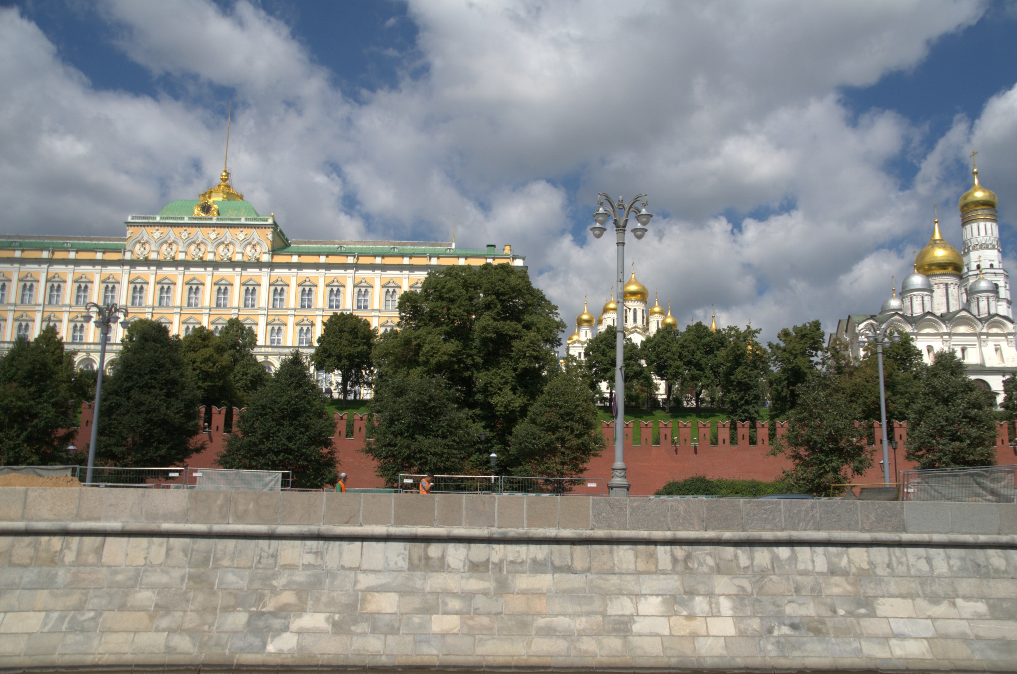 Erhabener Kreml in Moskau, Russland, mit ikonischen Gebäuden, Bäumen, Straßenlaternen, Straßenlaternen und einer umgebenden Wand unter einem bewölkten Himmel.