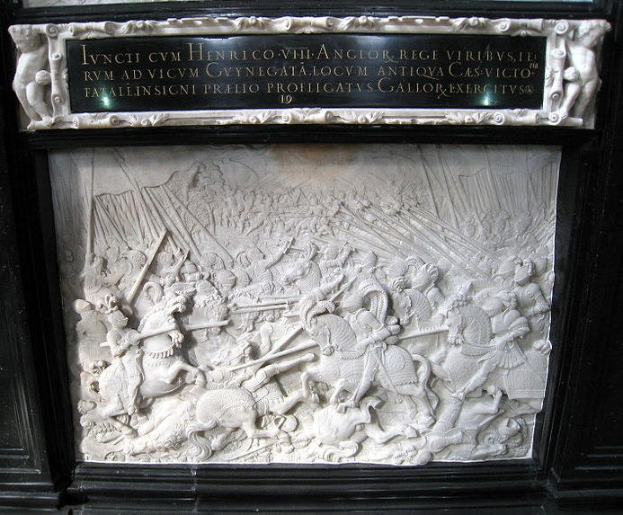 Weißer Marmorplakette an der Seite eines Gebäudes, die eine Kampfszene mit Figuren zeigt, die Schwerter und Schilde halten, umrahmt von einem schwarzen Rand, umgeben von Zuschauern.