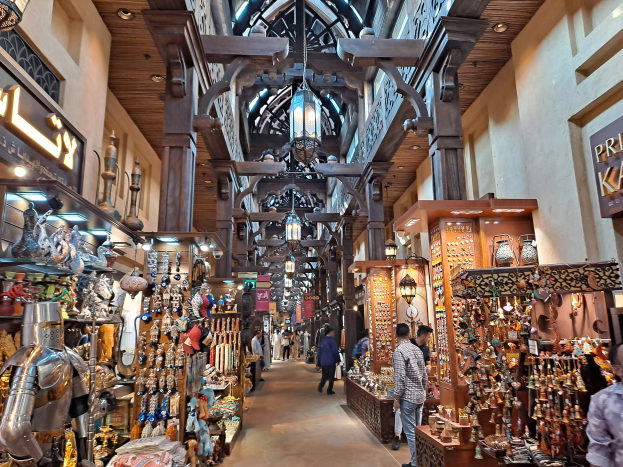 Ein belebter Dubai-Basar mit Menschen zwischen Gestellen mit Gegenständen, Wänden mit Text und einer Decke mit warmem Licht.