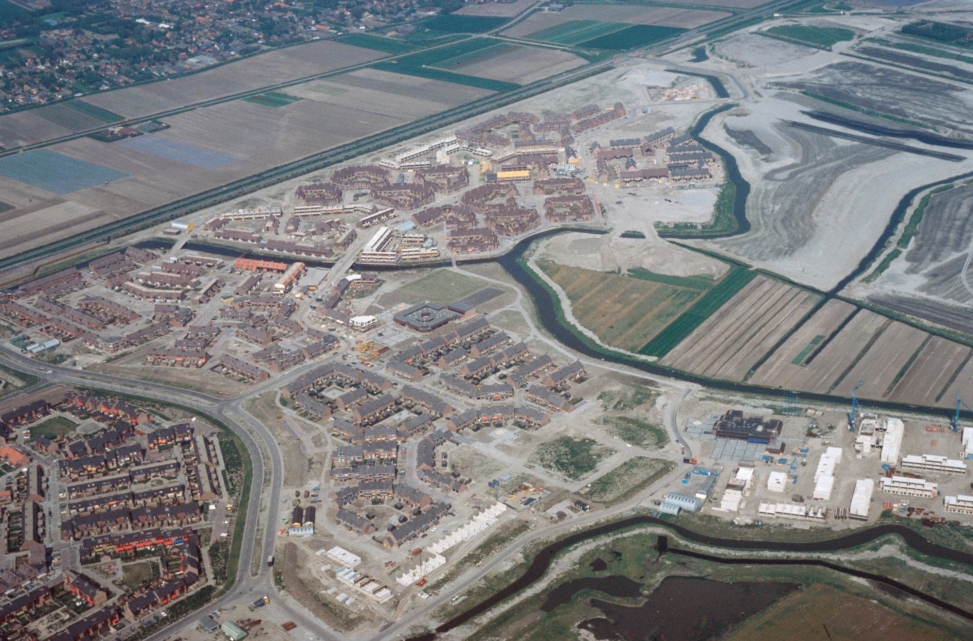 Luftaufnahme einer Stadt mit dichtem Baumbestand, Straßen, Grünflächen, Bäumen und einem zentralen Reservoir umgeben von städtischer Infrastruktur.