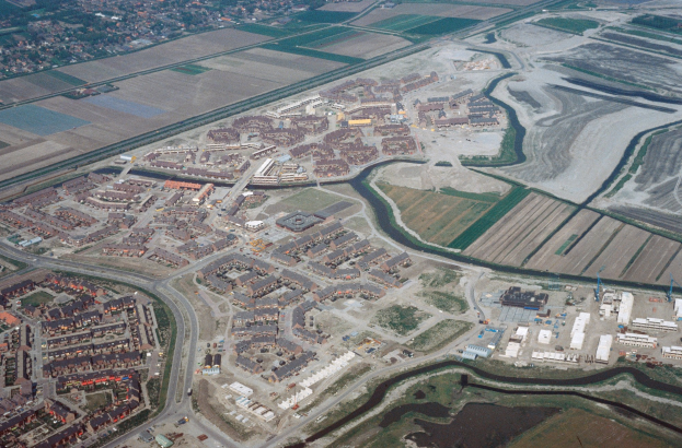 Luftaufnahme einer Stadt mit dichtem Baumbestand, Straßen, Grünflächen, Bäumen und einem zentralen Reservoir umgeben von städtischer Infrastruktur.